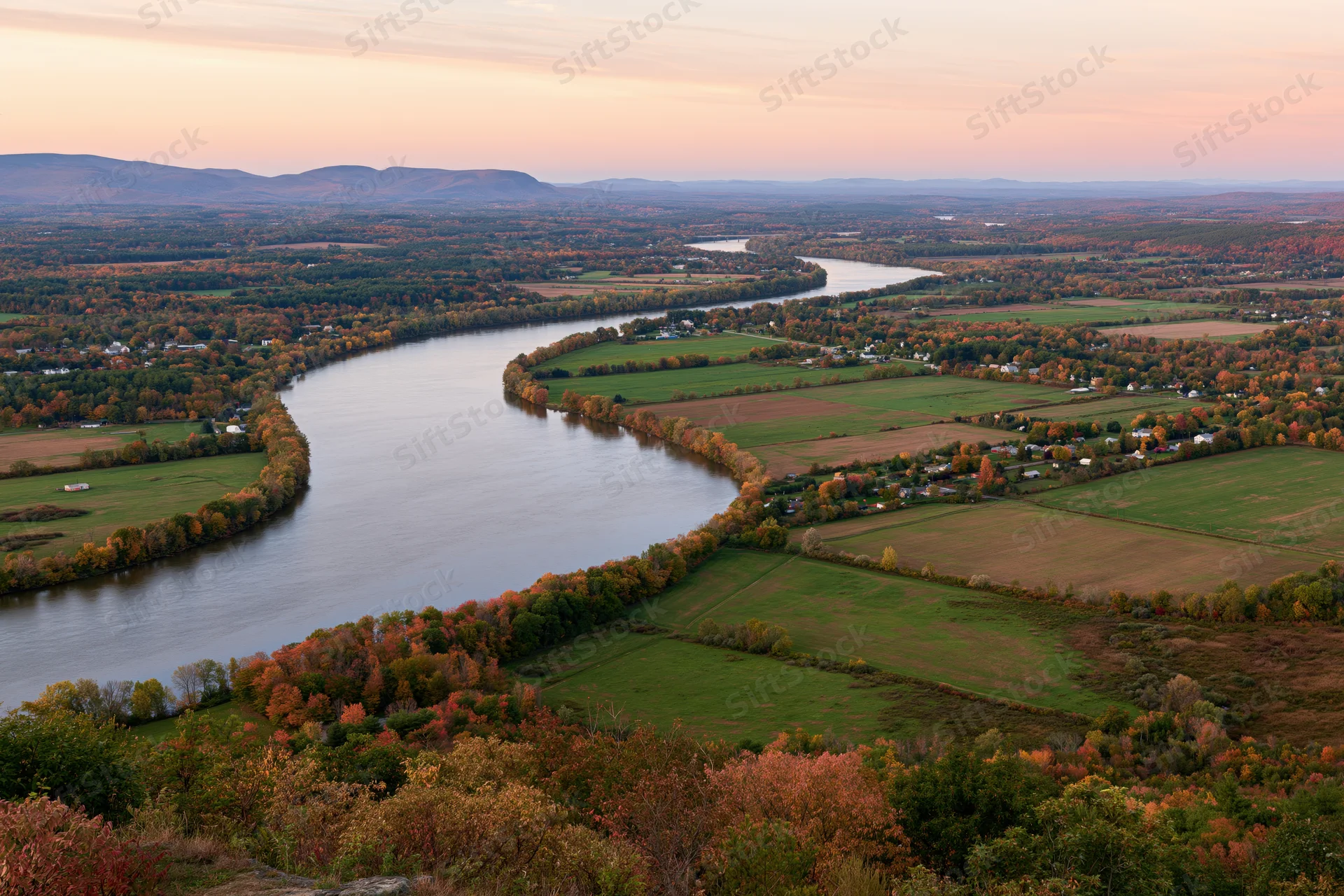 Aerial view of a wide river meandering through autumn-colored forests and farmland in new england