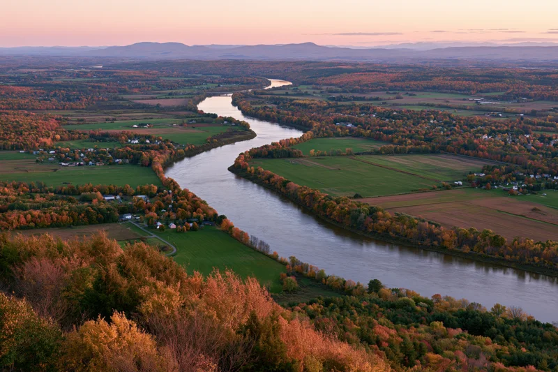 Aerial view of a wide river curving through autumn-colored forests and farmland in new england