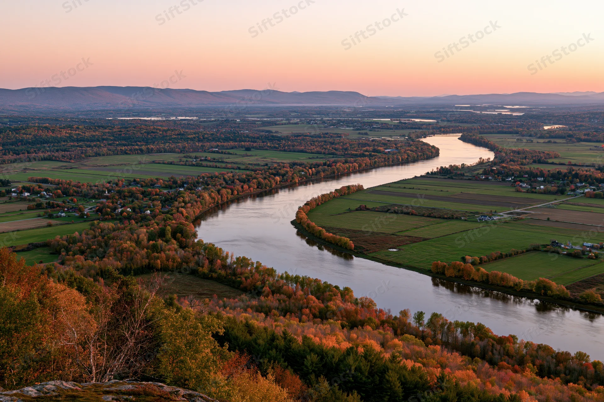 Aerial view of a wide river curving through a broad valley with autumn foliage and farmland in new england at sunset