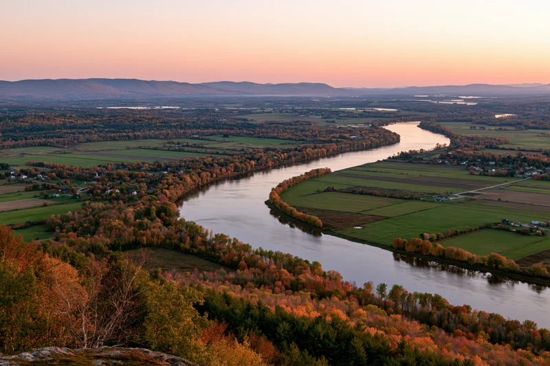 Aerial view of a wide river curving through a broad valley with autumn foliage and farmland in new england at sunset