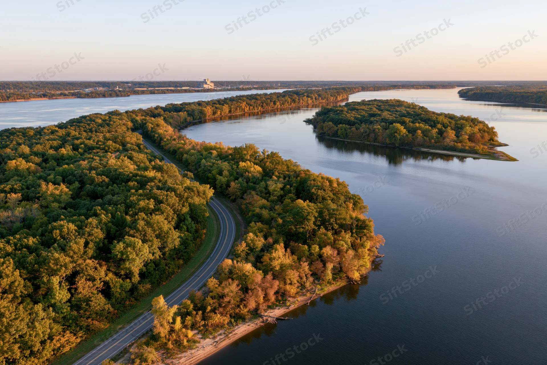 Aerial view of a winding river flowing through forested islands with a curving road along the shore