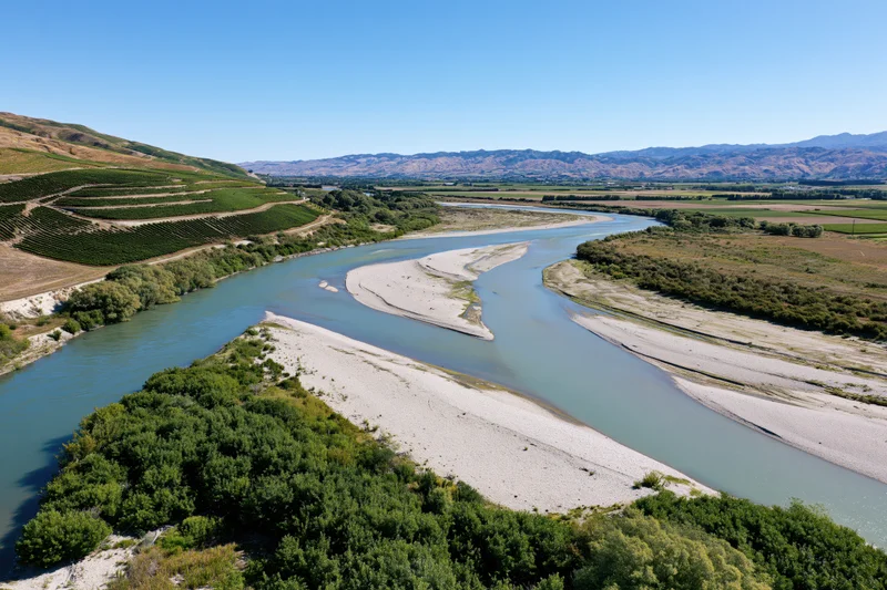 Aerial view of a winding river with sandy banks cutting through vineyards and valleys under a clear blue sky