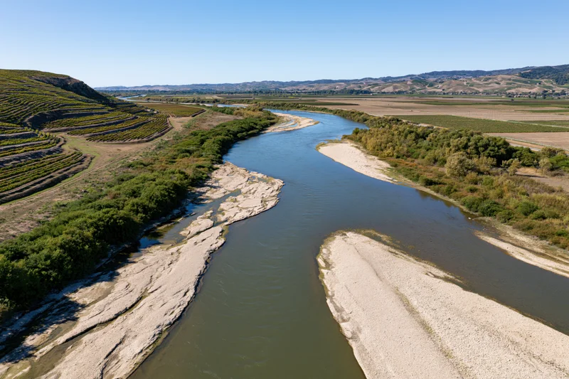 Aerial view of a winding river with sandy banks cutting through vineyards and farmland in a valley