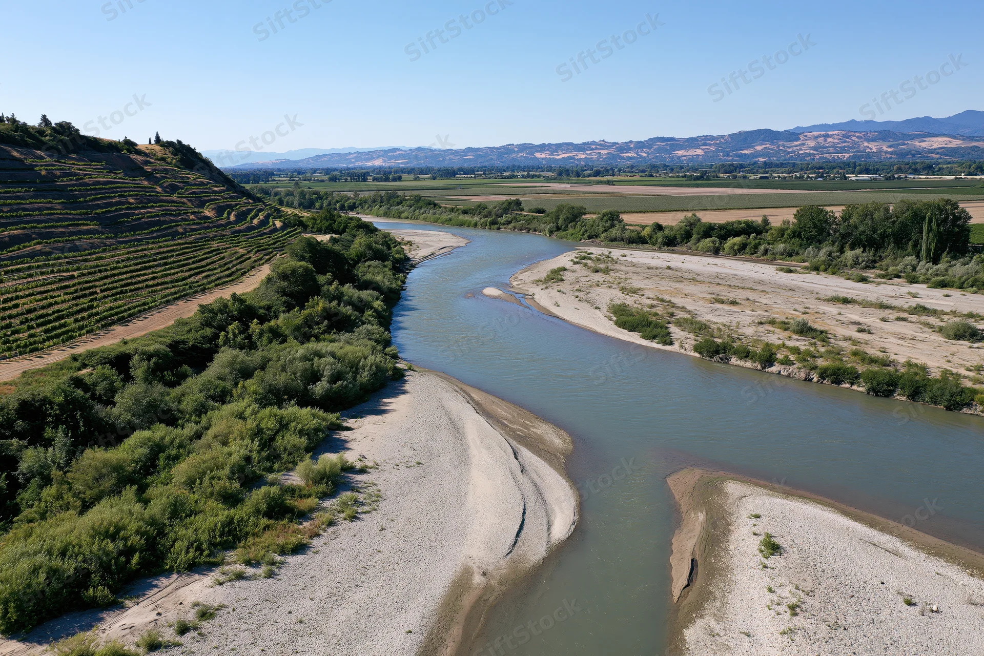 Aerial view of a winding river with sandy banks cutting through vineyards and farmland in a valley