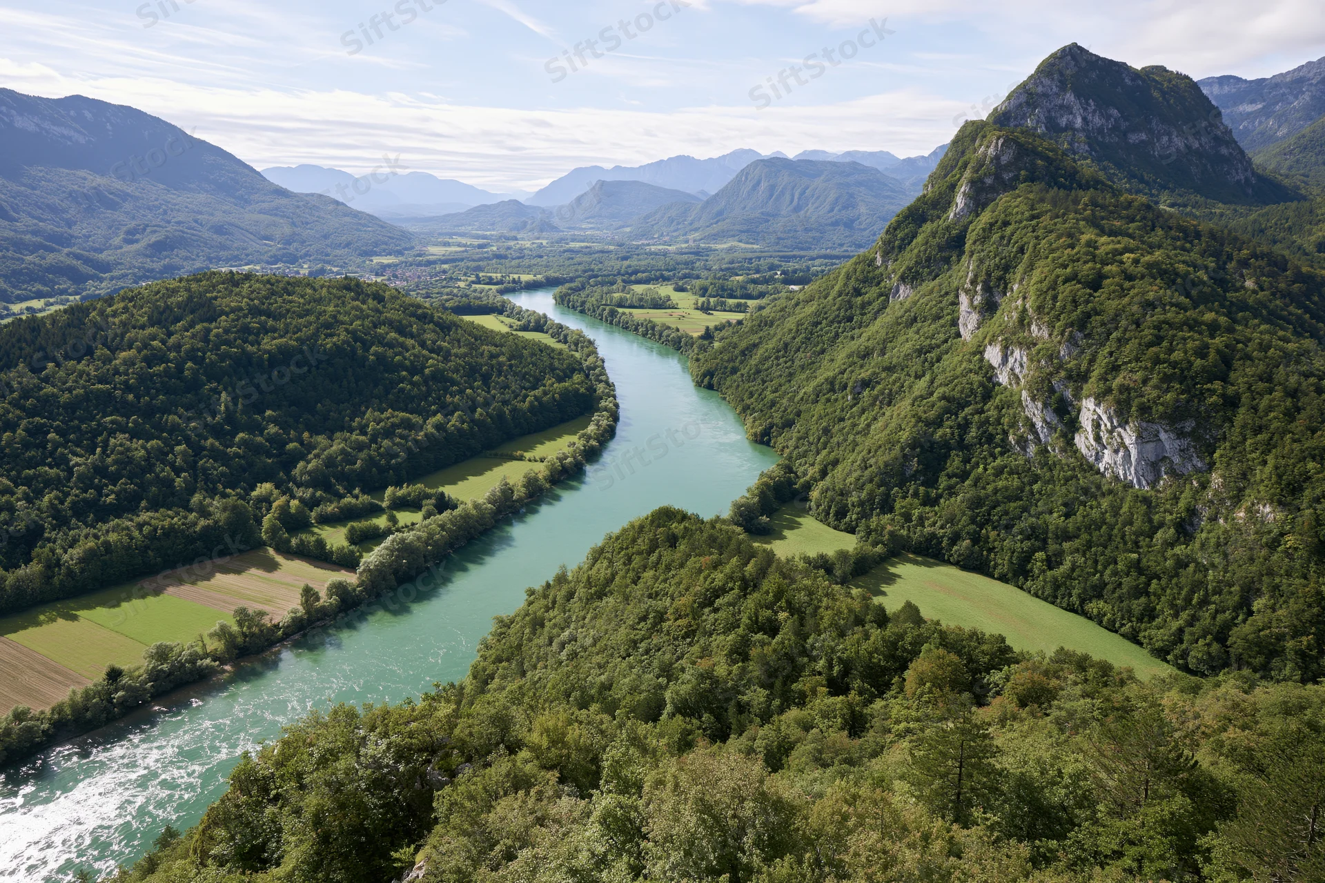 Aerial view of a winding river with turquoise-green water flowing through a forested valley surrounded by mountains