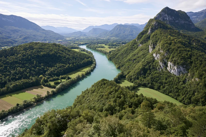 Aerial view of a winding river with turquoise-green water flowing through a forested valley surrounded by mountains
