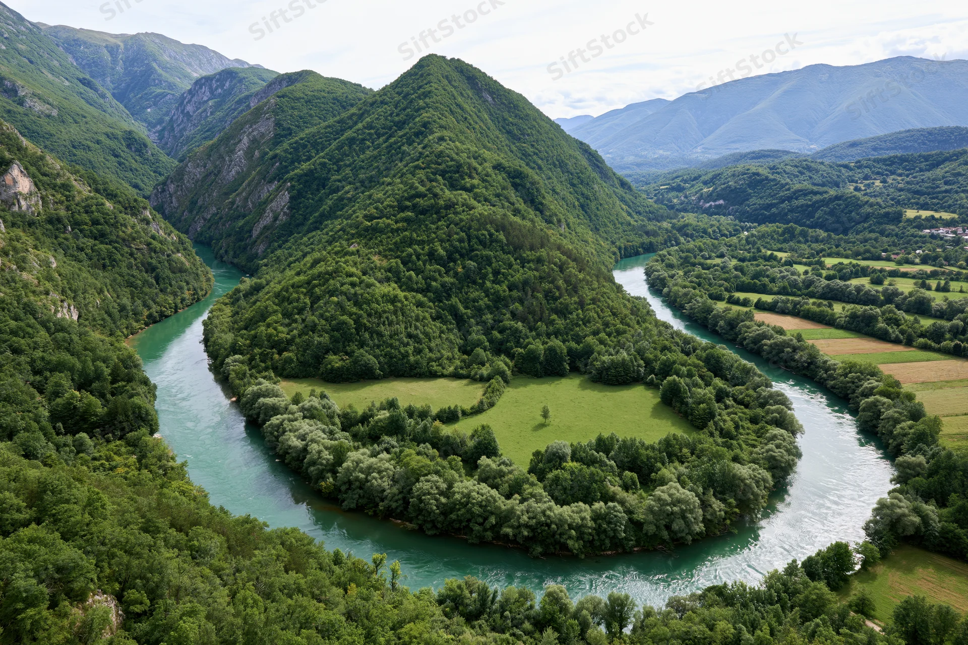 Aerial view of a winding river with turquoise-green water snaking through forested mountains and valleys