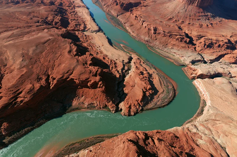 Aerial view of a winding turquoise river flowing through a red rock canyon