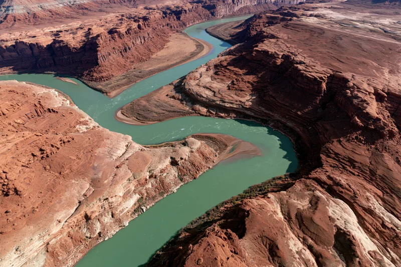 Aerial view of a winding turquoise river flowing through a red rock canyon