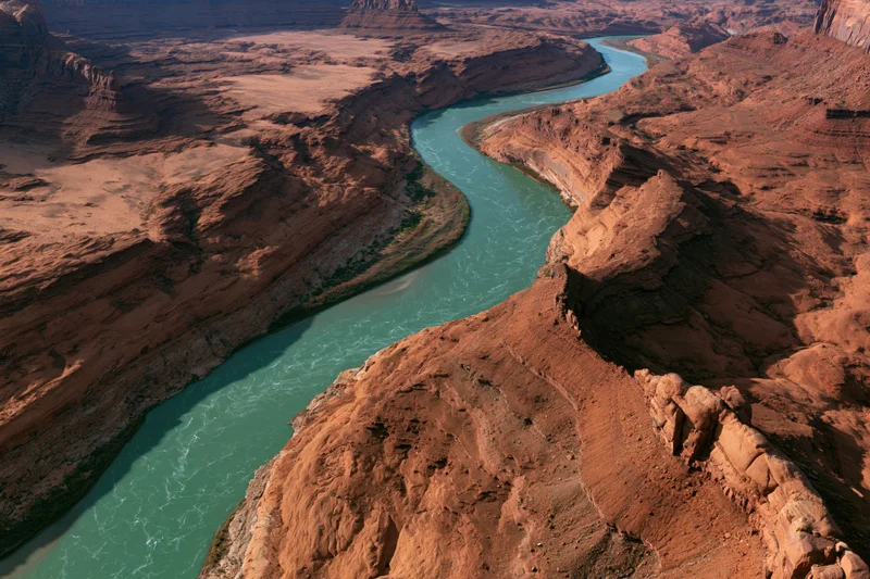 Aerial view of a winding turquoise river flowing through a red rock canyon in a desert landscape