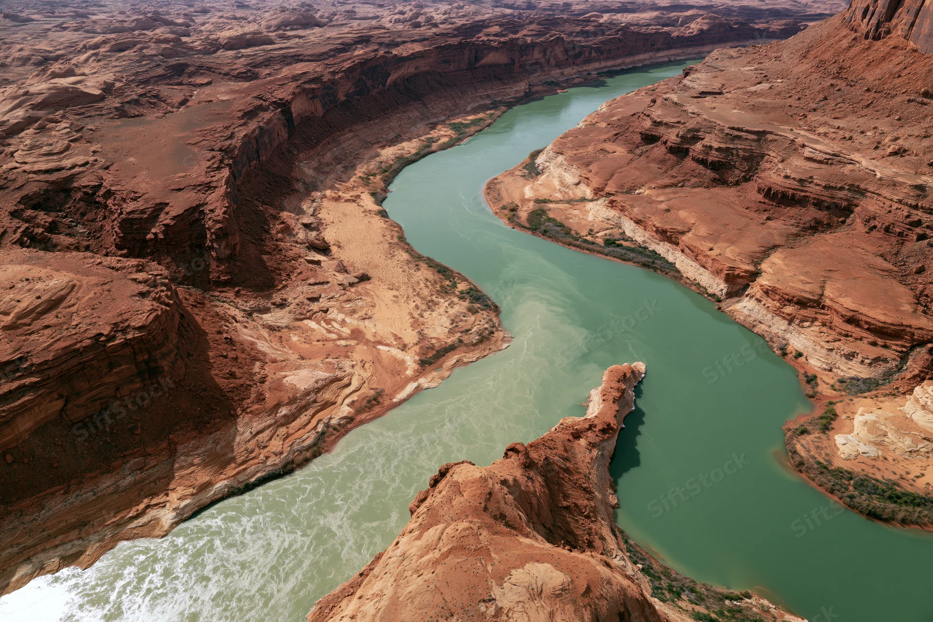Aerial view of a winding turquoise river flowing through a deep red rock canyon
