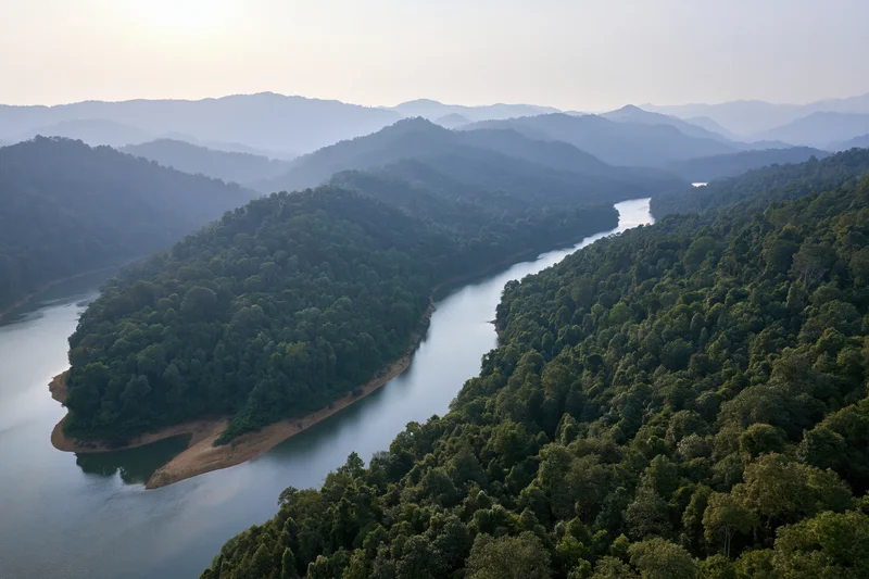 Aerial view of a winding river cutting through dense tropical forest surrounded by mountains
