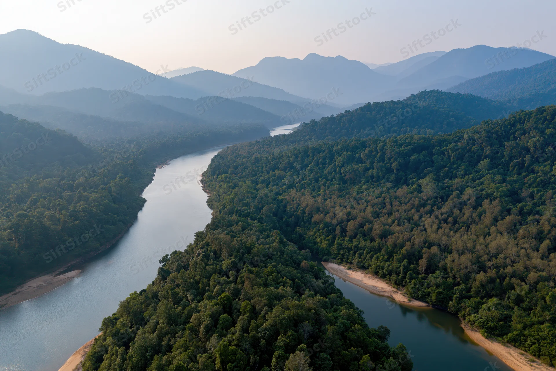 Aerial view of a winding river cutting through dense tropical forest surrounded by mountains