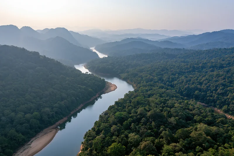 Aerial view of a winding river cutting through dense tropical forest surrounded by mountains
