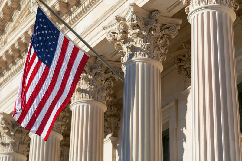 American flag waving on diagonal pole attached to neoclassical government building facade with corinthian columns
