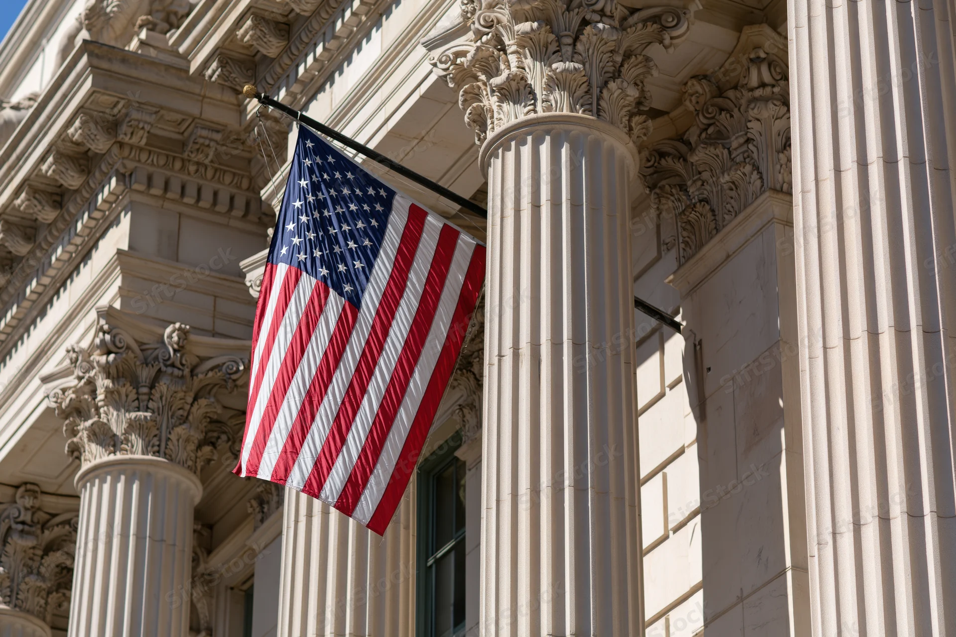 American flag on diagonal pole attached to classical stone building facade with corinthian columns