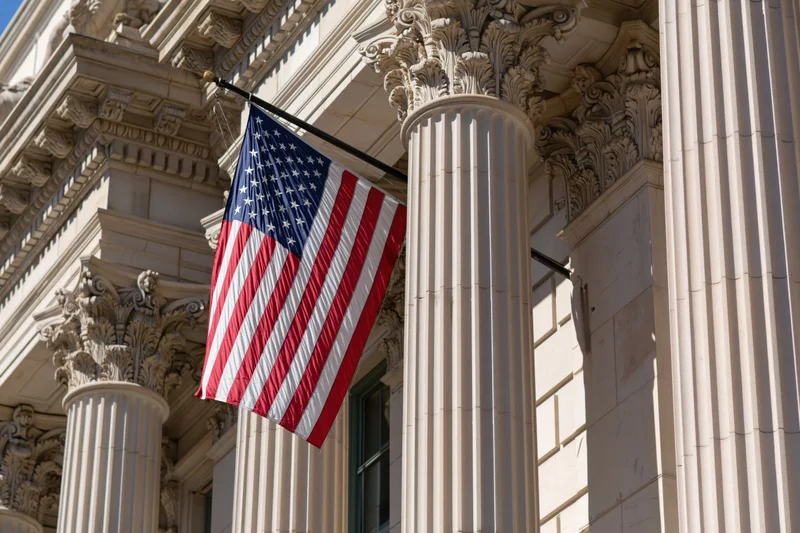American flag on diagonal pole attached to classical stone building facade with corinthian columns