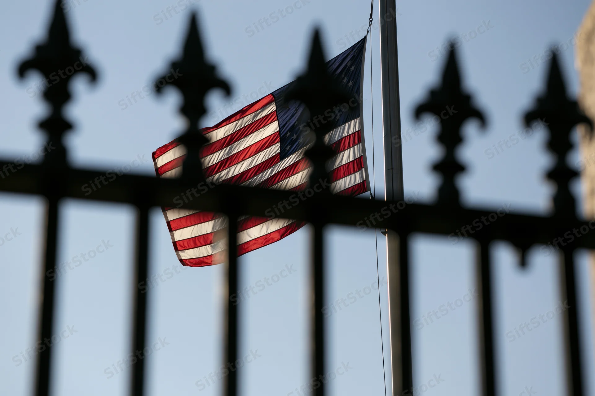 American flag waving in breeze behind wrought iron fence against sky