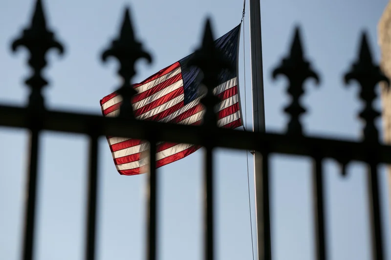 American flag waving in breeze behind wrought iron fence against sky