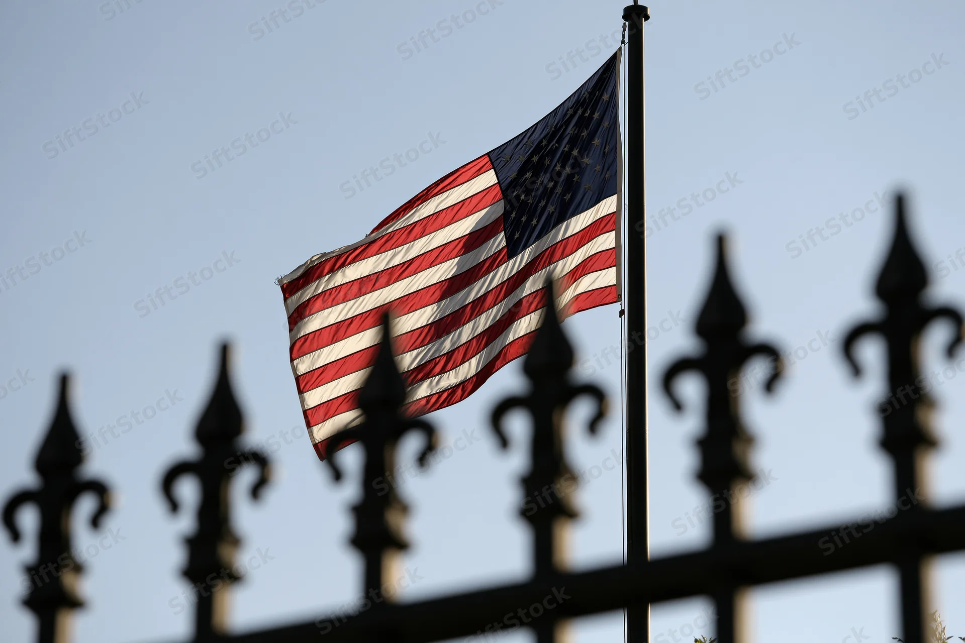 American flag waving in breeze on tall pole behind wrought iron fence