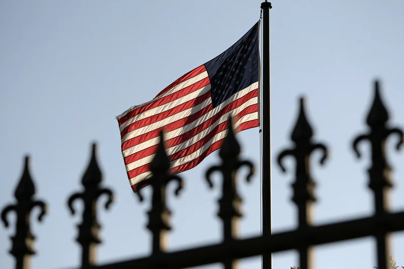 American flag waving in breeze on tall pole behind wrought iron fence