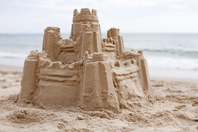 Elaborate sand castle with tiered towers and battlements on a sandy beach near the ocean