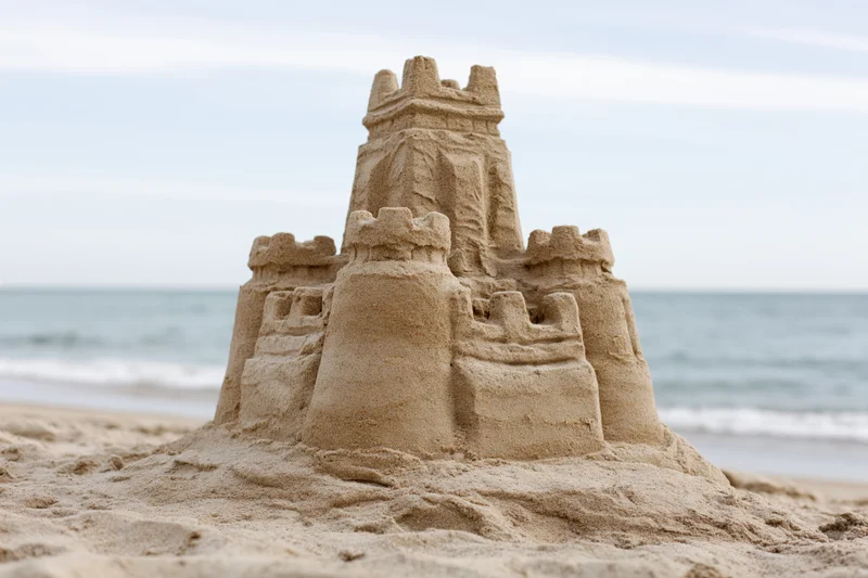 Elaborate sandcastle with tiered towers and battlements on a sandy beach near the ocean