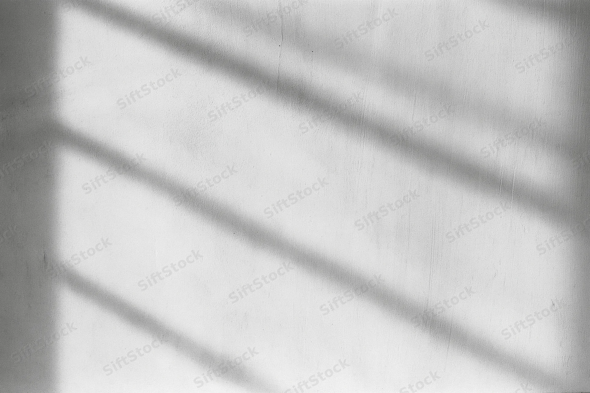 Diagonal shadows from window blinds cast on a bare concrete wall