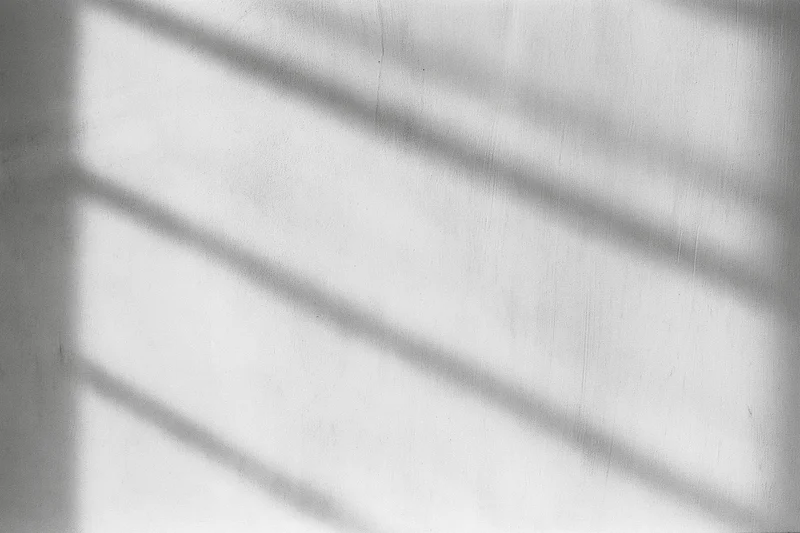 Diagonal shadows from window blinds cast on a bare concrete wall