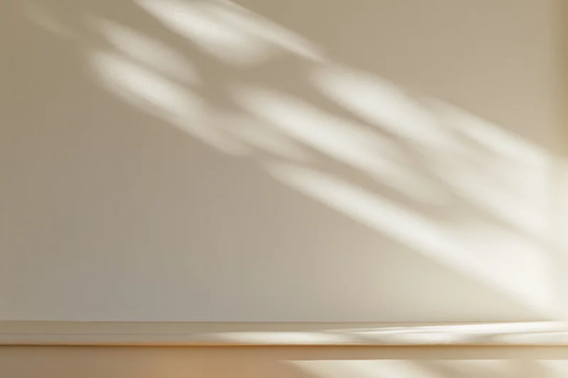 Cream-white plaster wall with soft sunlight casting diagonal shadows across smooth matte surface in indoor room setting