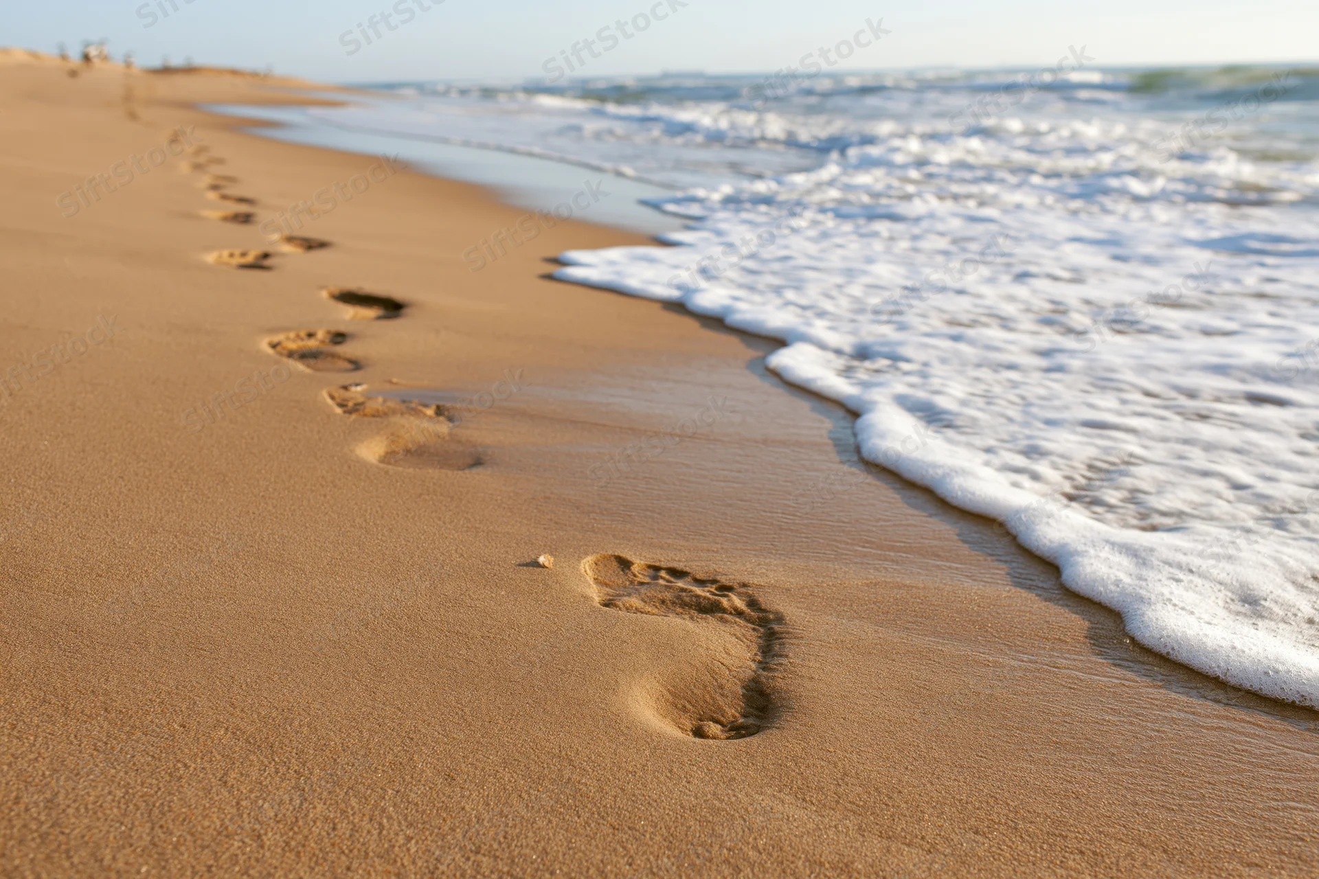 Footprints in wet golden sand leading diagonally toward the ocean shoreline