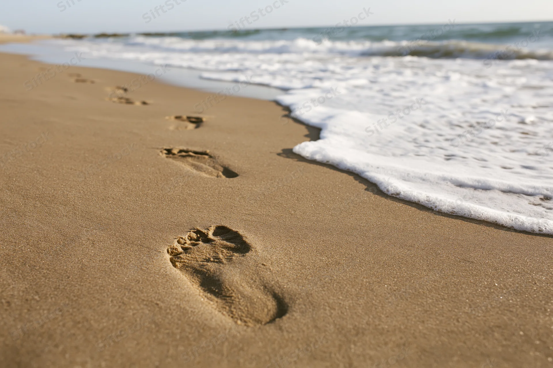 Footprints in wet golden sand leading toward ocean waves at shoreline