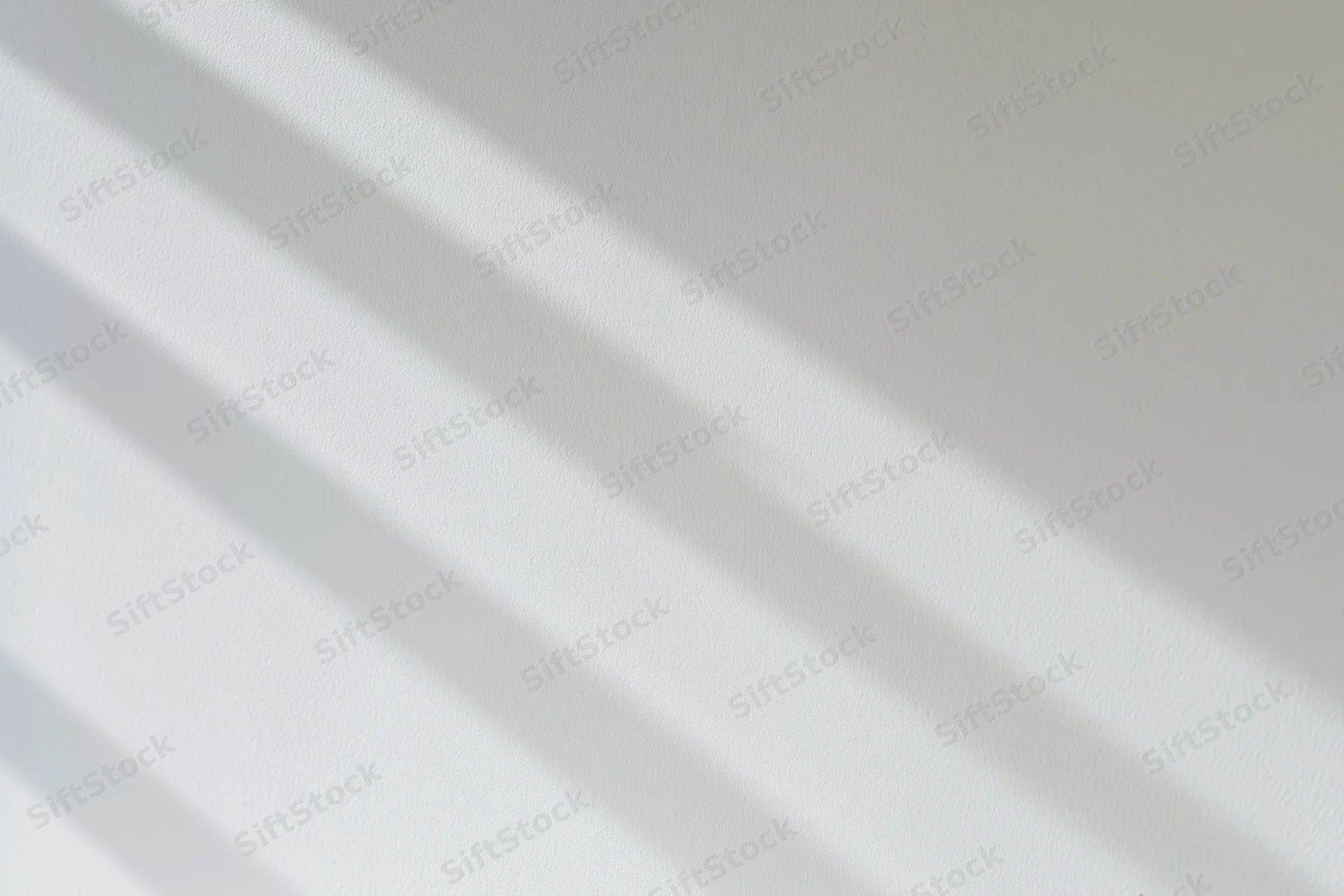 Diagonal shadows from blinds on a white plaster wall