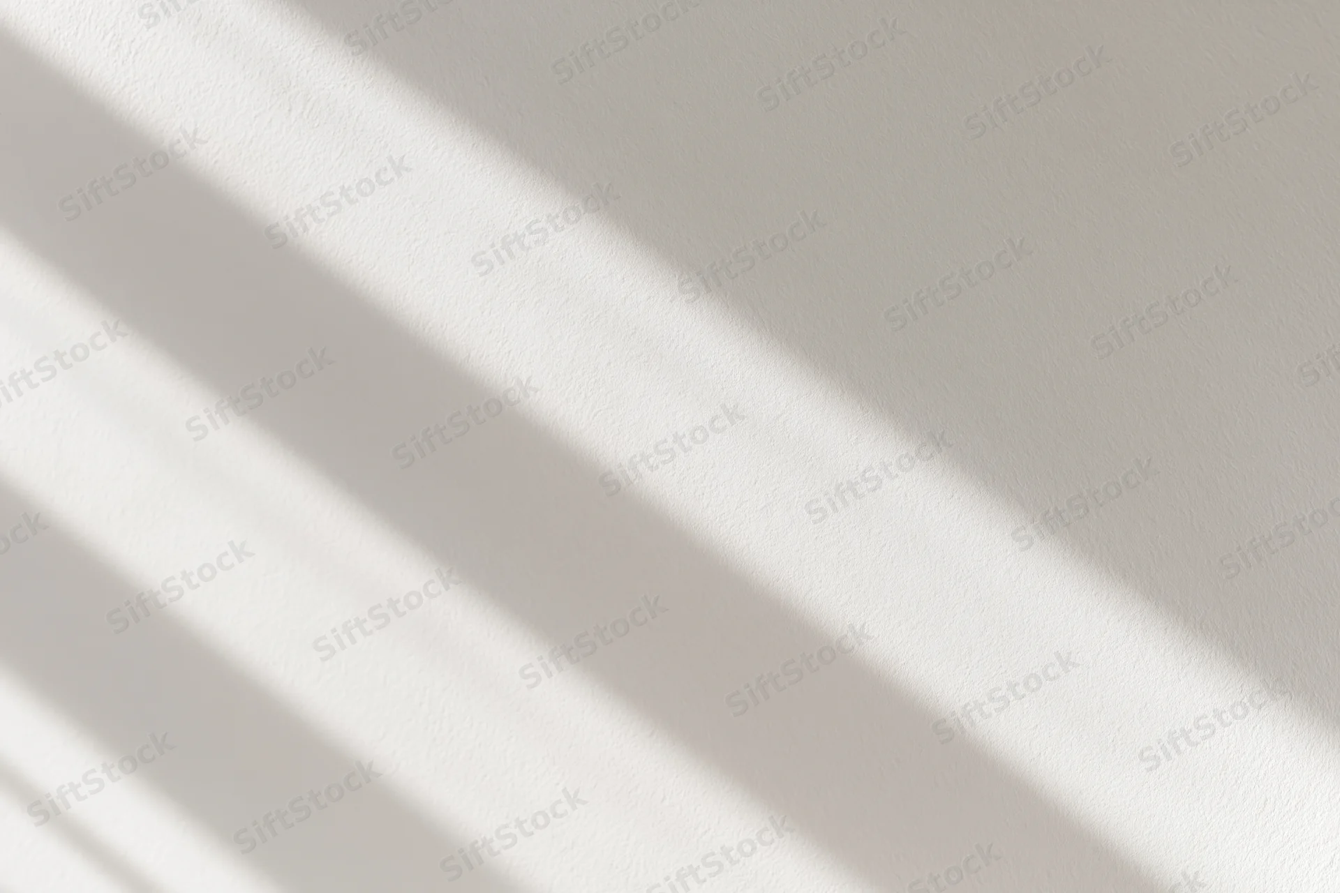 Diagonal light and shadow stripes on a white plaster wall interior
