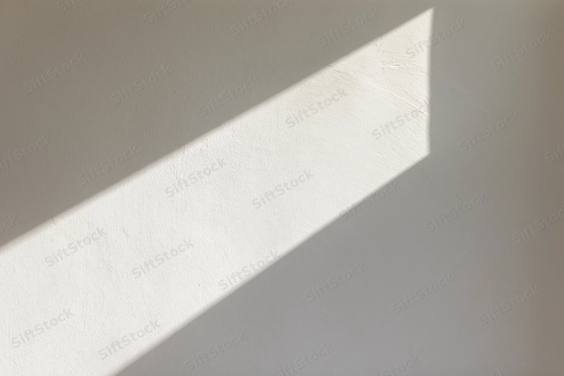 Diagonal beam of sunlight on a white plaster wall indoors