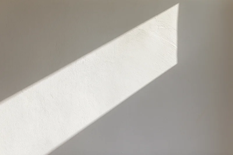 Diagonal beam of sunlight on a white plaster wall indoors