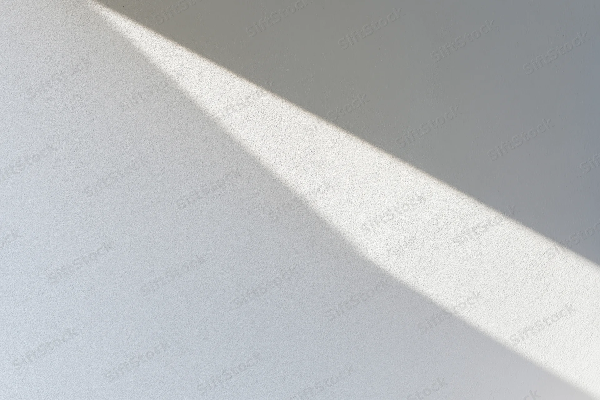 Diagonal sunlight casting a sharp shadow on a white plaster wall indoors