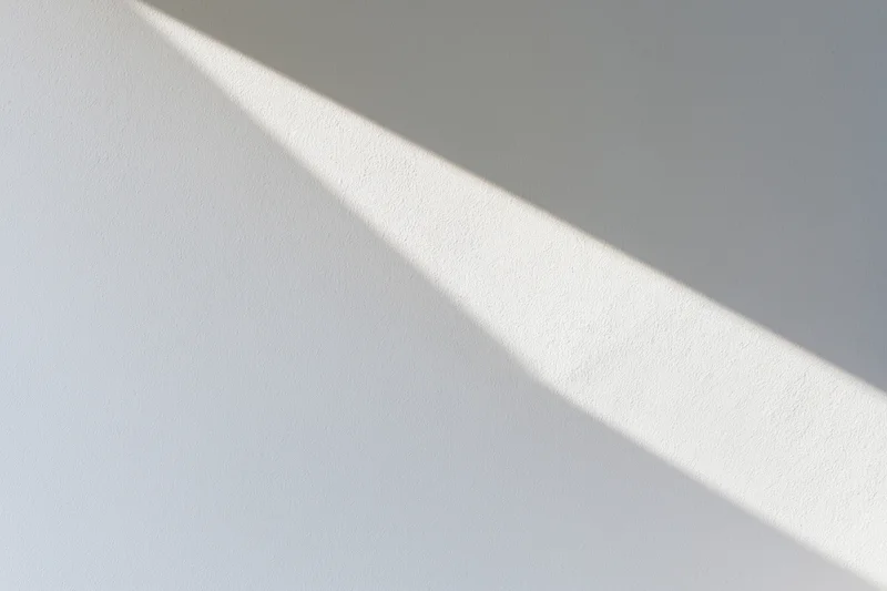Diagonal sunlight casting a sharp shadow on a white plaster wall indoors