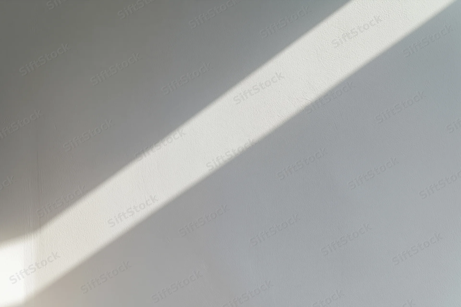Diagonal sunlight casting a bright stripe across a smooth white plaster wall in an empty interior space