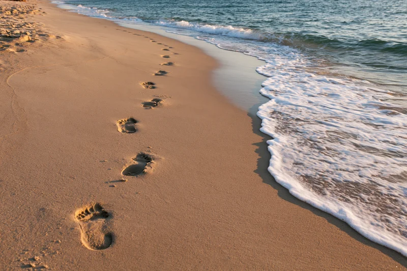 Footprints in wet golden sand along the shoreline with waves approaching