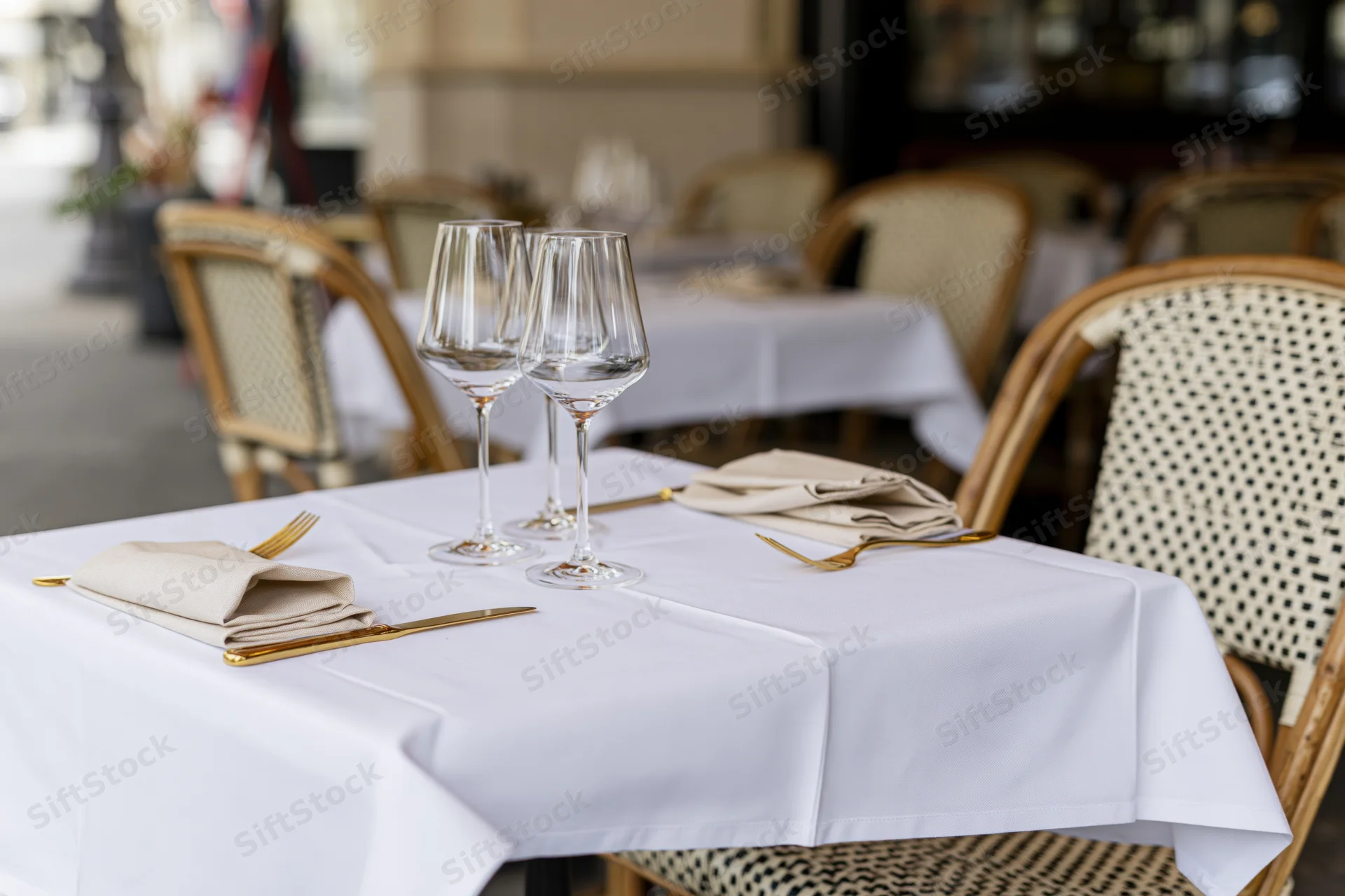 Bistro table set with white tablecloth, wine glasses, folded linen napkins and gold cutlery outdoors