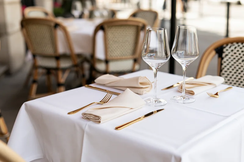 Bistro table set with wine glasses and gold cutlery on white linen napkins outdoors