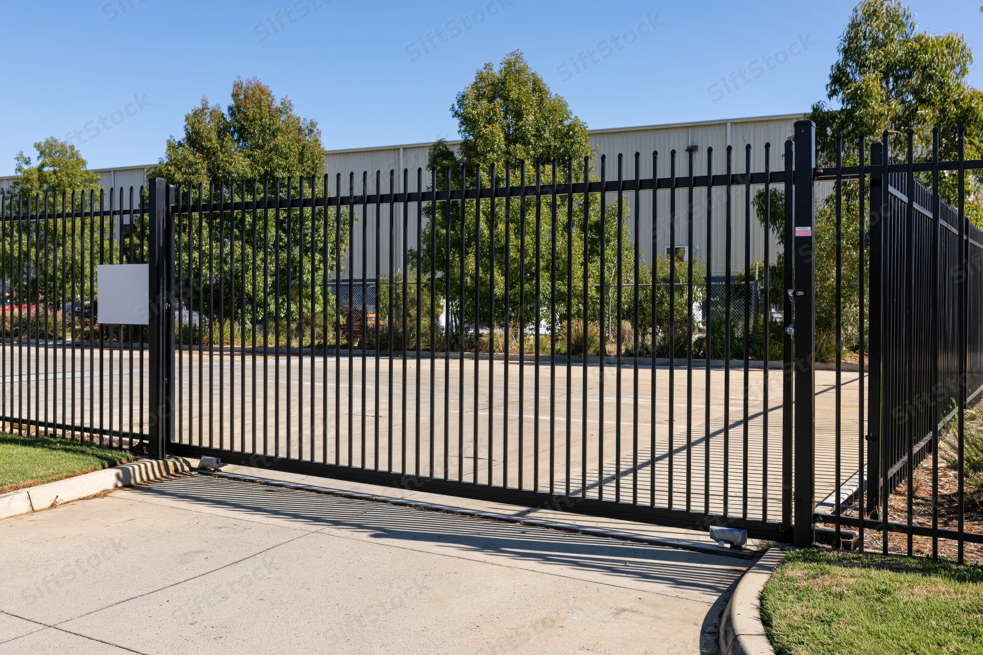 Black steel sliding security gate across concrete driveway in front of industrial building