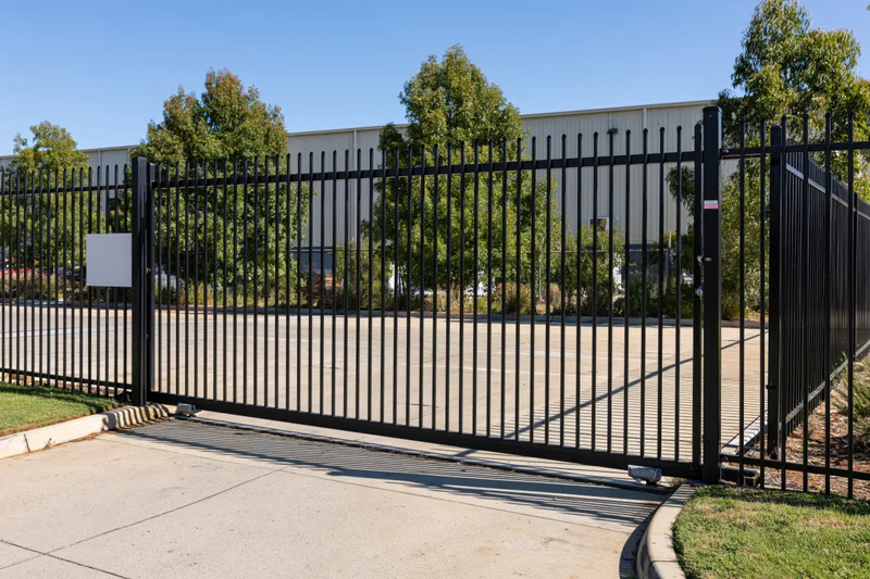 Black steel sliding security gate across concrete driveway in front of industrial building