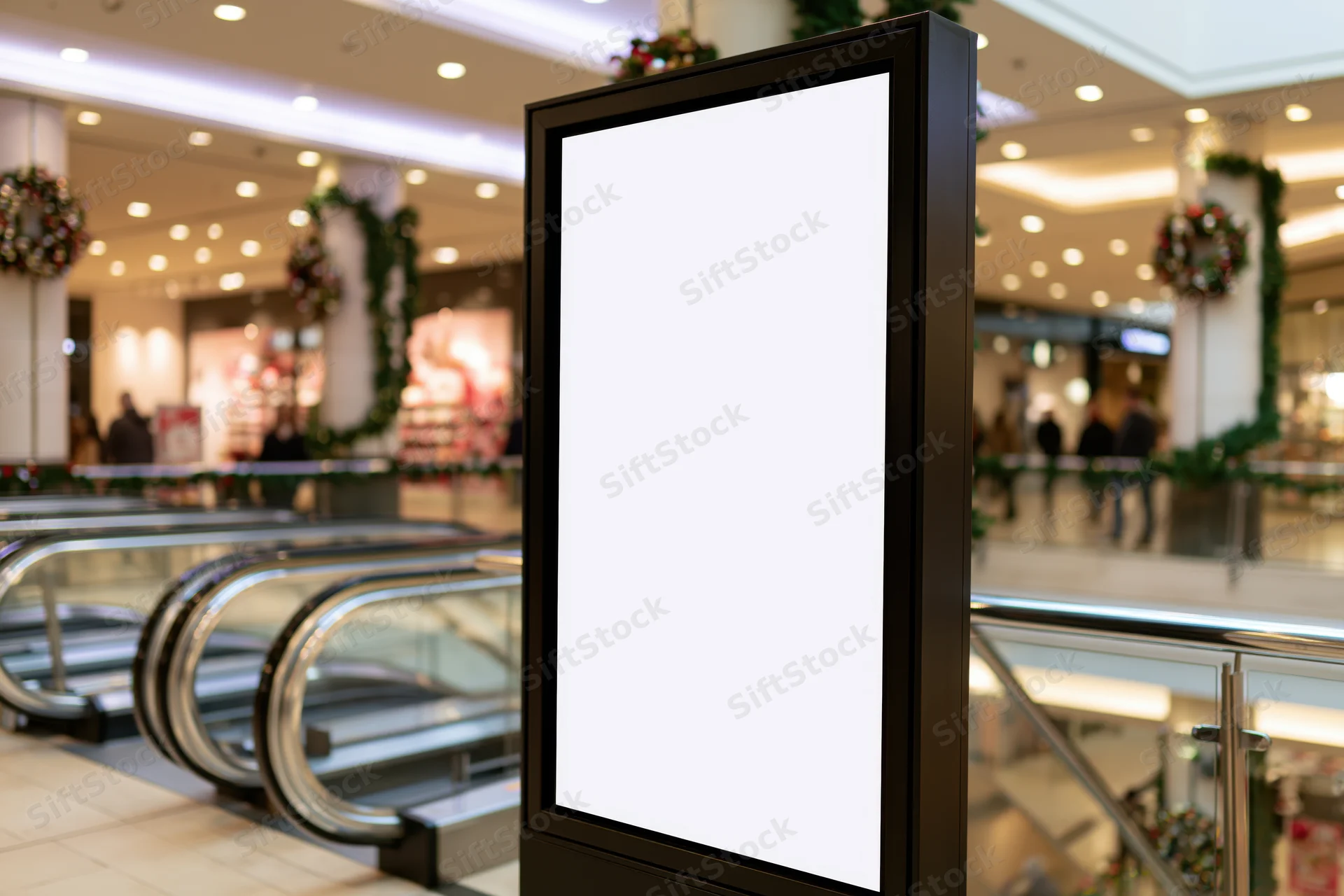 Blank vertical digital display kiosk in a decorated shopping mall interior near escalators