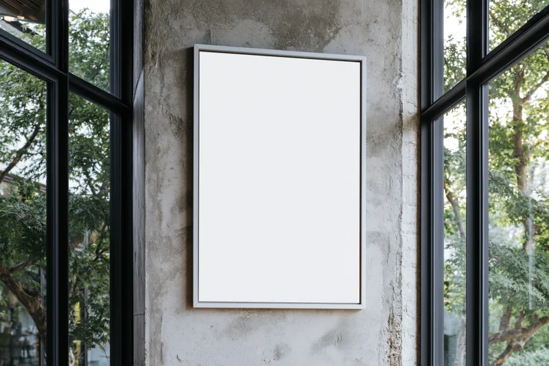 Blank white poster frame mounted on a raw concrete wall between glass windows
