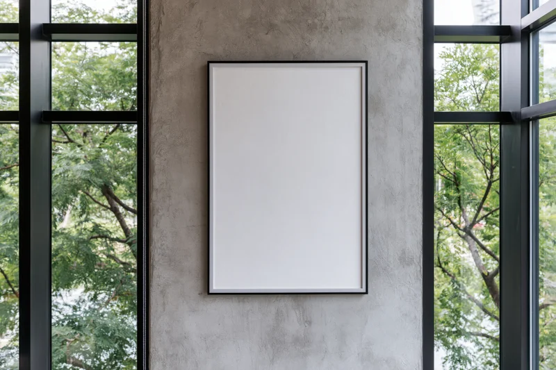 Blank white poster frame mounted on a concrete wall between glass windows in a modern interior