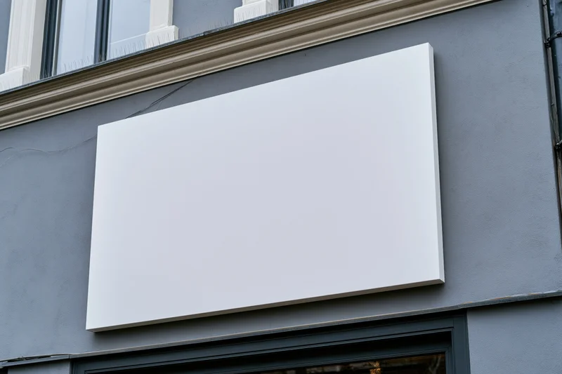 Blank white rectangular sign mounted on grey building facade above shop window