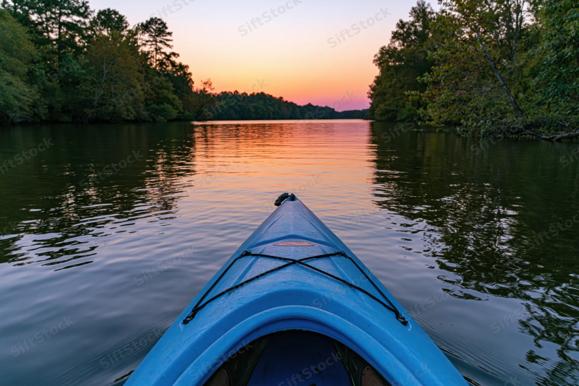 Blue kayak bow pointing forward on calm river at sunset surrounded by forest