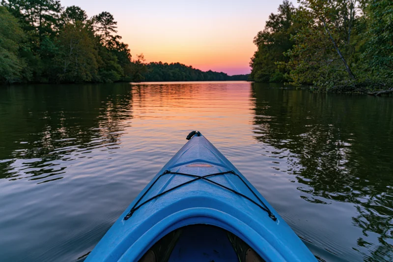 Blue kayak bow pointing forward on calm river at sunset surrounded by forest